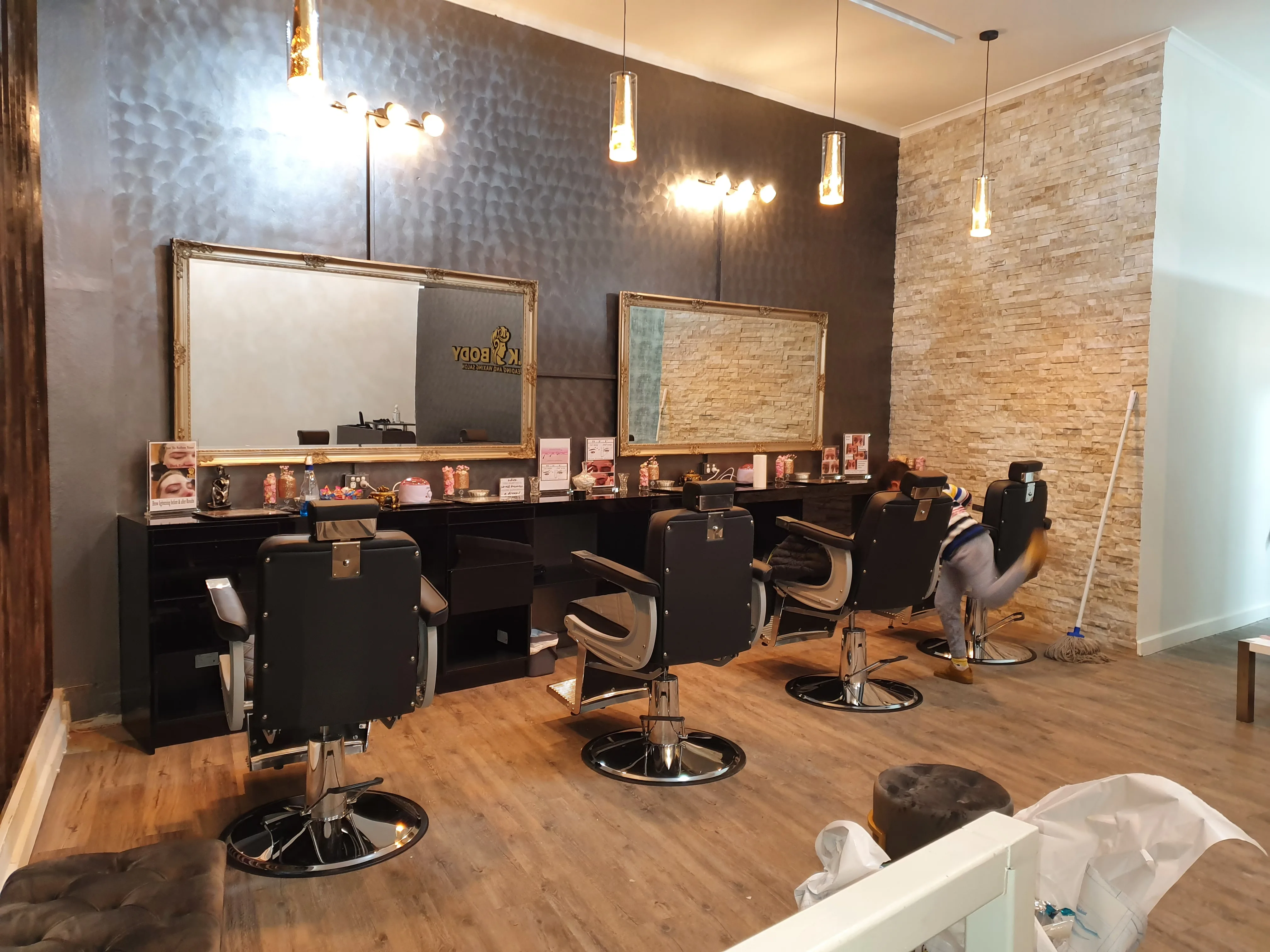 Silk Body salon interior — a row of black styling chairs beneath ornate gold-framed mirrors, warm pendant light, charcoal feature wall